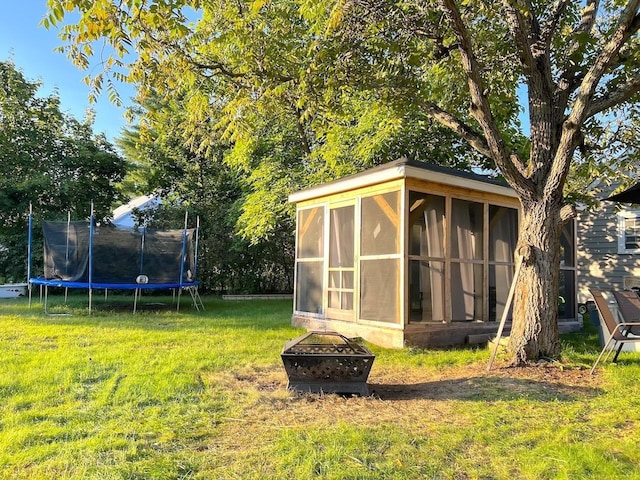 view of outdoor structure with a trampoline, an outdoor fire pit, and a sunroom