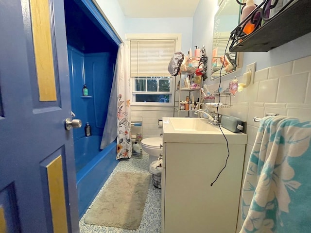 bathroom featuring toilet, shower / bath combo with shower curtain, vanity, and tile walls