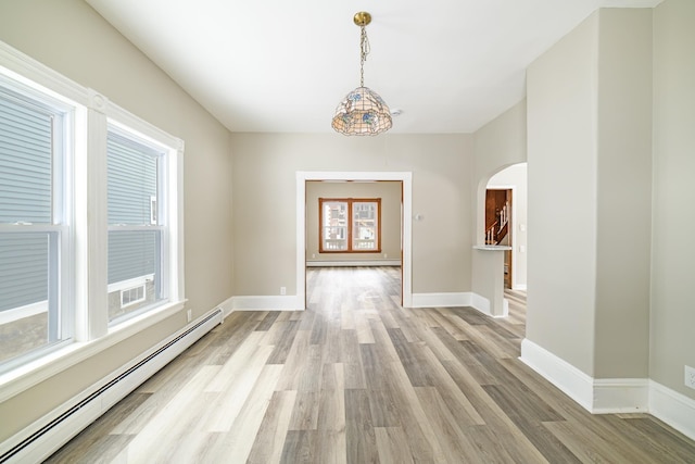 interior space with arched walkways, baseboard heating, and a healthy amount of sunlight