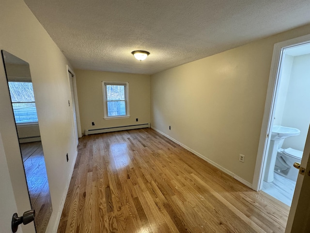 interior space featuring a textured ceiling, baseboard heating, and light wood-style floors