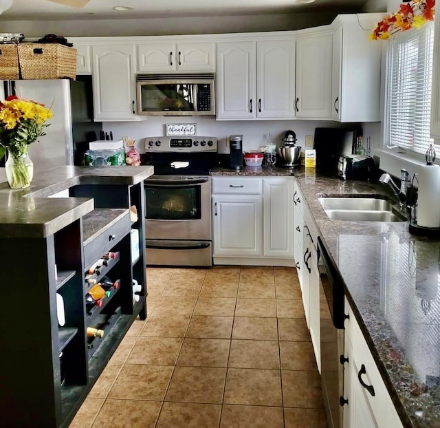 kitchen featuring dark stone counters, appliances with stainless steel finishes, white cabinetry, a sink, and light tile patterned flooring