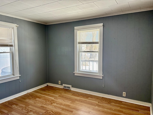 spare room featuring ornamental molding, light wood-type flooring, visible vents, and baseboards