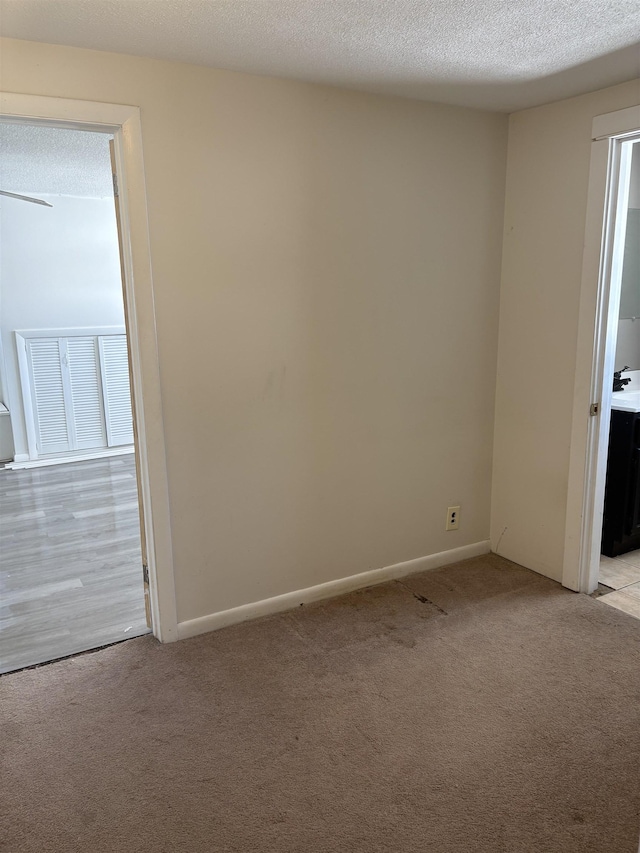 spare room featuring light carpet, a textured ceiling, visible vents, and baseboards