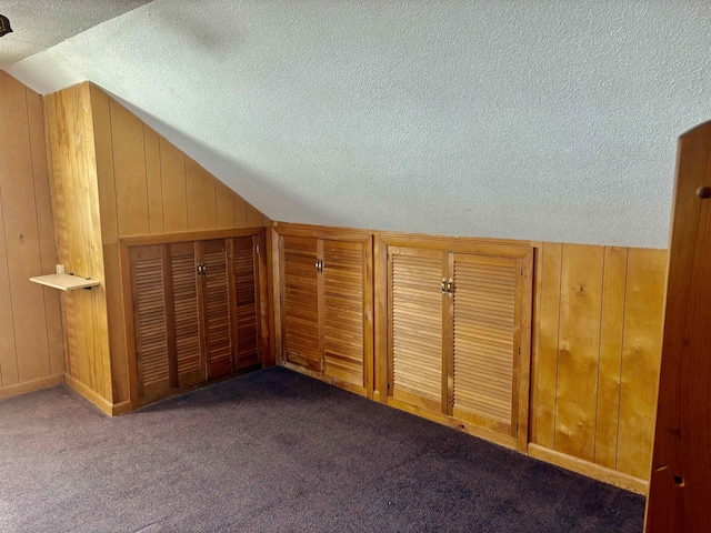 bonus room featuring lofted ceiling, carpet, wooden walls, and a textured ceiling