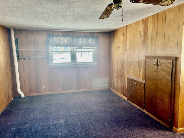 carpeted spare room featuring wood walls, baseboards, a ceiling fan, and a textured ceiling