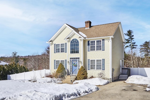 view of front of house featuring a shingled roof, a chimney, and fence