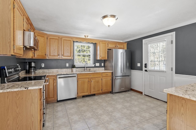 kitchen featuring light stone counters, stainless steel appliances, a sink, wainscoting, and crown molding