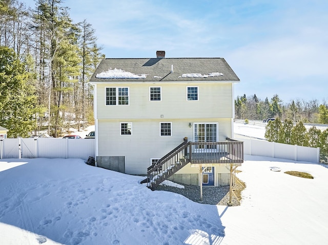 snow covered property featuring a deck, fence, stairs, a gate, and a chimney