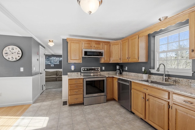 kitchen featuring light tile patterned floors, appliances with stainless steel finishes, light stone counters, ornamental molding, and a sink