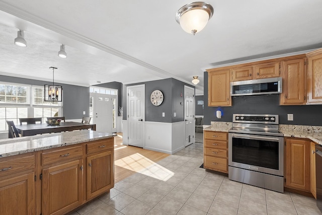 kitchen featuring crown molding, light tile patterned floors, hanging light fixtures, appliances with stainless steel finishes, and light stone countertops