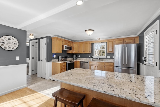 kitchen with light stone counters, stainless steel appliances, ornamental molding, a sink, and a kitchen bar