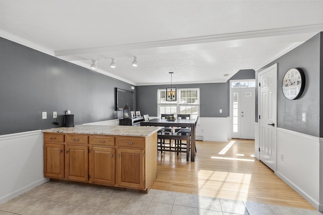 kitchen featuring crown molding, light wood finished floors, hanging light fixtures, brown cabinetry, and a peninsula