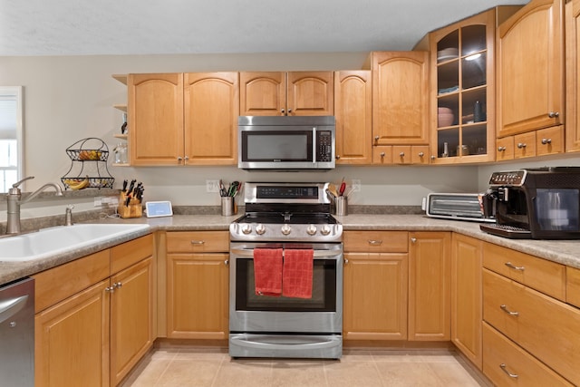 kitchen with glass insert cabinets, light tile patterned floors, appliances with stainless steel finishes, and a sink