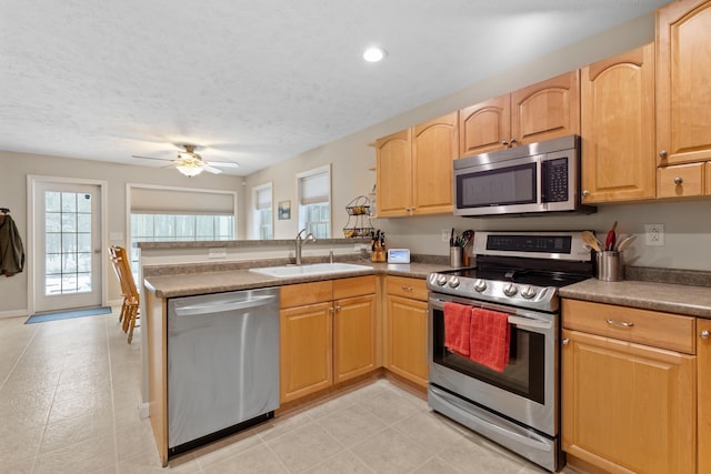 kitchen featuring a peninsula, stainless steel appliances, a textured ceiling, light brown cabinetry, and a sink