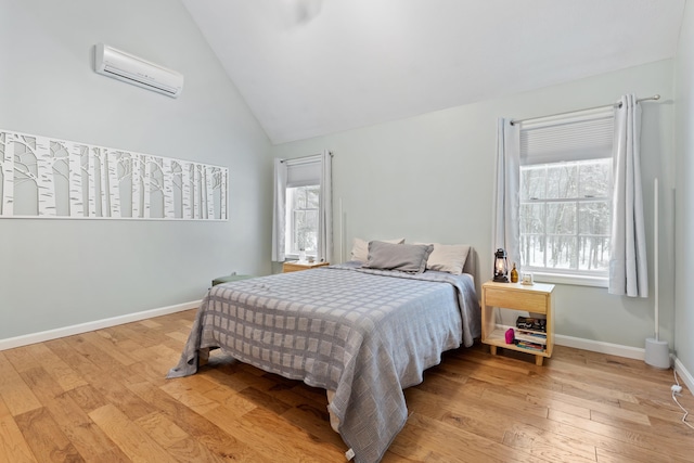 bedroom with light wood-style floors, baseboards, vaulted ceiling, and a wall mounted AC