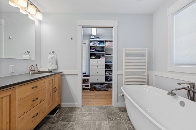 full bath featuring a soaking tub, radiator heating unit, a spacious closet, and vanity