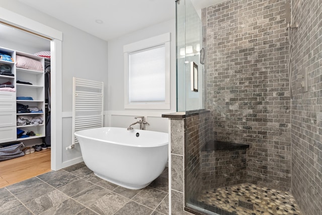 bathroom featuring a stall shower, wainscoting, radiator heating unit, a spacious closet, and a freestanding tub