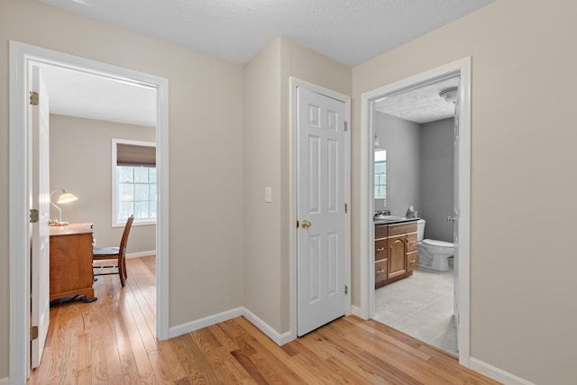 corridor featuring a textured ceiling, light wood finished floors, a sink, and baseboards