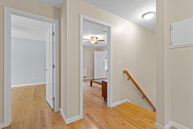 corridor featuring a textured ceiling, light wood finished floors, an upstairs landing, and baseboards