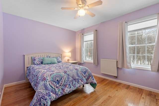 bedroom featuring multiple windows, radiator heating unit, and wood finished floors