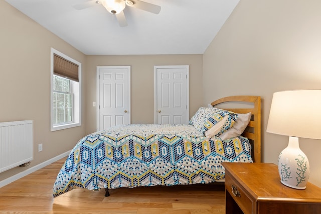 bedroom featuring two closets, radiator, a ceiling fan, wood finished floors, and baseboards