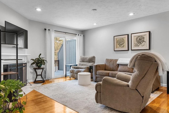 living area with a textured ceiling, recessed lighting, a fireplace with flush hearth, wood finished floors, and baseboards