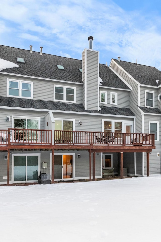 snow covered property featuring a shingled roof and a chimney