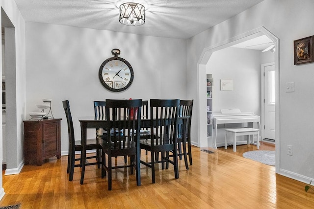 dining space featuring arched walkways, a textured ceiling, wood finished floors, and baseboards