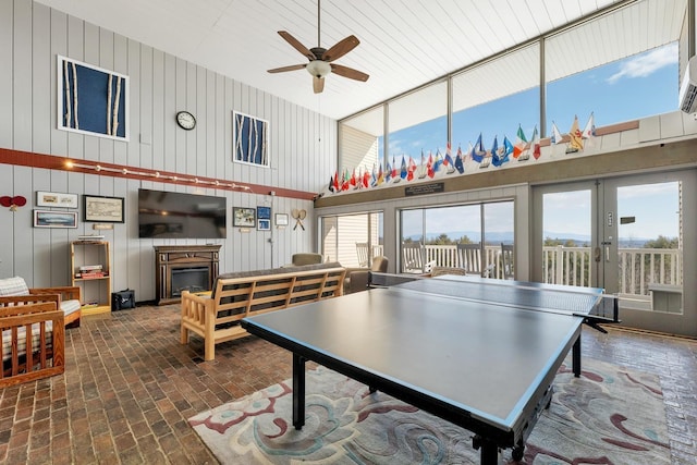 recreation room featuring french doors, a high ceiling, a fireplace, brick floor, and ceiling fan