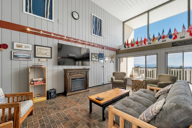 living room with brick floor, a wealth of natural light, a glass covered fireplace, and a towering ceiling