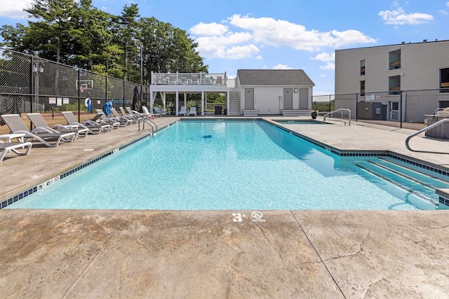 community pool with a patio, fence, and an outbuilding