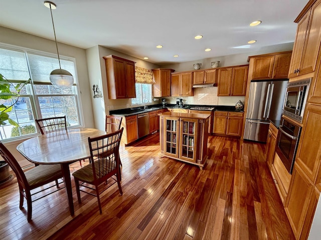 kitchen featuring brown cabinetry, dark countertops, dark wood-style floors, appliances with stainless steel finishes, and a sink