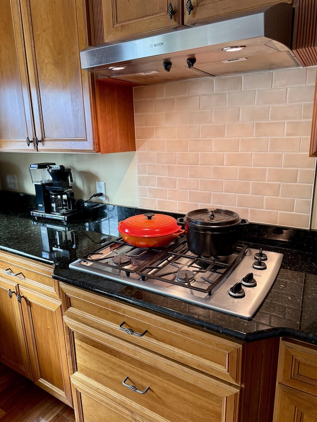 kitchen featuring dark stone counters, stainless steel gas stovetop, decorative backsplash, and extractor fan