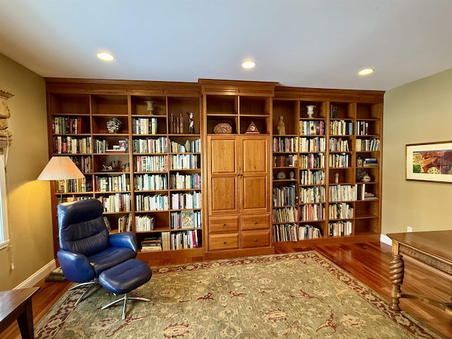 sitting room with wall of books, baseboards, wood finished floors, and recessed lighting