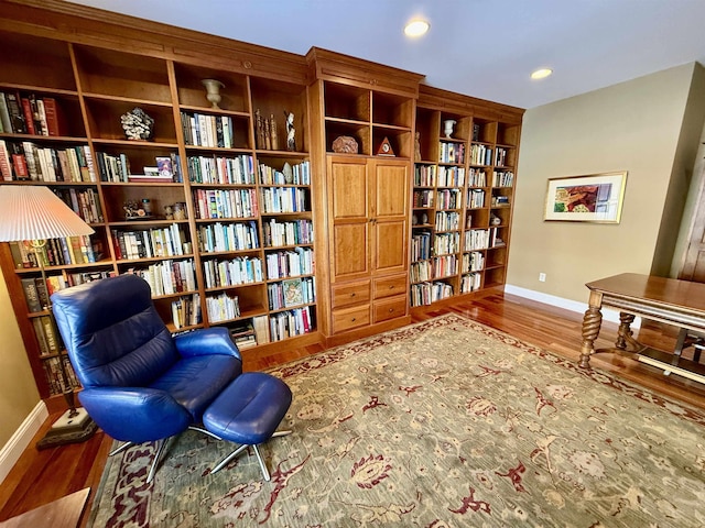 sitting room with wall of books, baseboards, wood finished floors, and recessed lighting