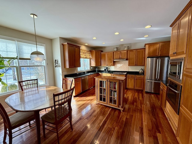 kitchen featuring stainless steel appliances, a sink, brown cabinets, dark wood-style floors, and dark countertops