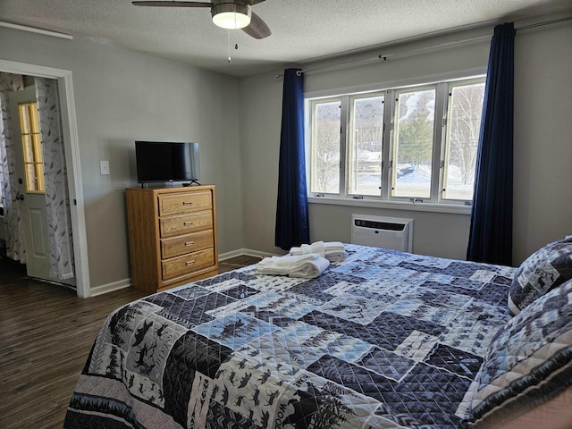 bedroom with dark wood finished floors, a ceiling fan, a textured ceiling, a wall mounted air conditioner, and baseboards