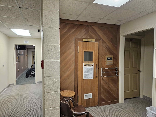 interior space featuring baseboards, carpet flooring, wooden walls, and a drop ceiling