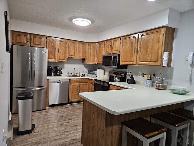 kitchen with appliances with stainless steel finishes, brown cabinets, a peninsula, light countertops, and a sink