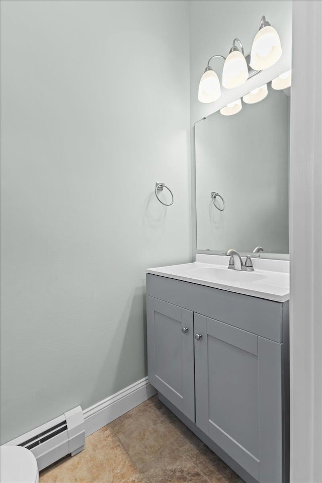 half bathroom featuring a baseboard heating unit, toilet, vanity, and baseboards