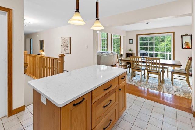 kitchen with light tile patterned floors, a center island, open floor plan, hanging light fixtures, and light stone countertops