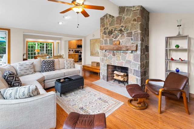 living area with a ceiling fan, a fireplace, vaulted ceiling, and wood finished floors