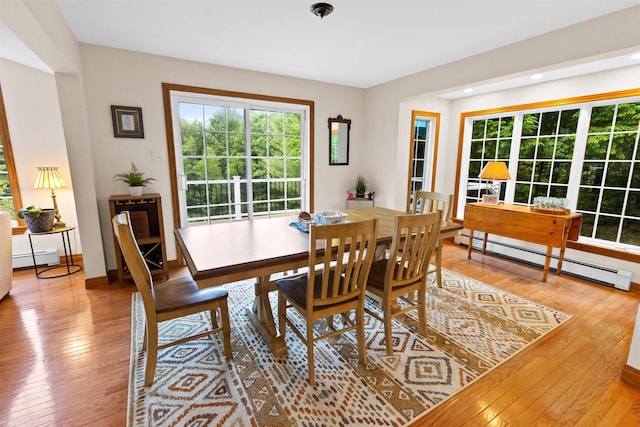 dining room with a baseboard heating unit, baseboards, and light wood finished floors