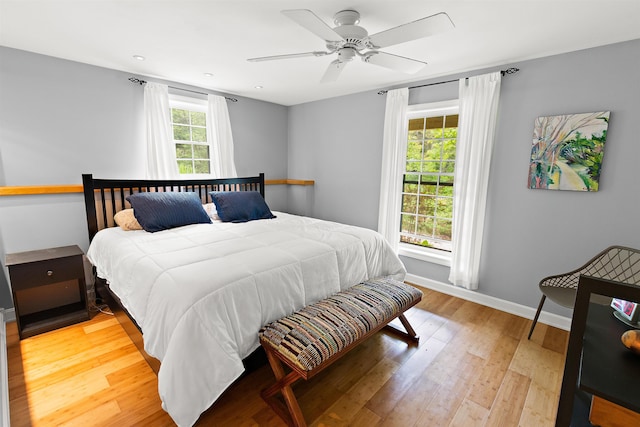 bedroom with baseboards, multiple windows, a ceiling fan, and light wood-style floors