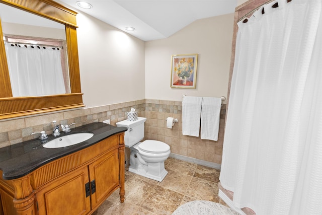 bathroom featuring toilet, a wainscoted wall, vaulted ceiling, vanity, and tile walls