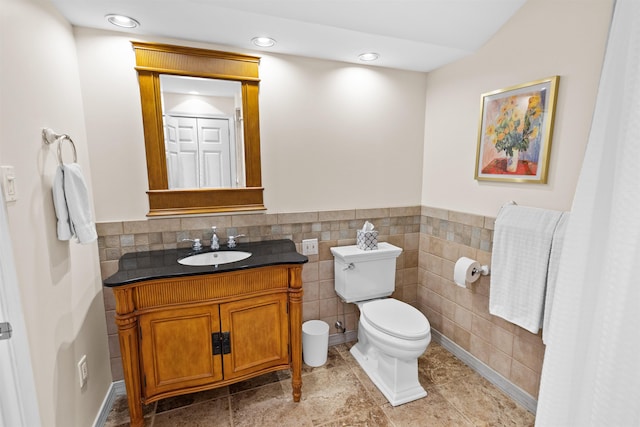 bathroom featuring toilet, recessed lighting, tile walls, vanity, and wainscoting