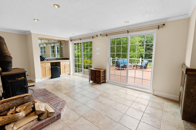 living area featuring a wood stove, a healthy amount of sunlight, crown molding, and baseboards