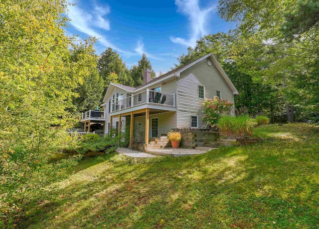 back of house featuring a patio area, a lawn, a chimney, and a wooden deck