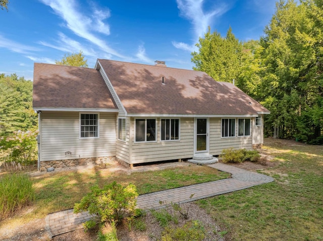 back of property with a yard, a shingled roof, and a chimney