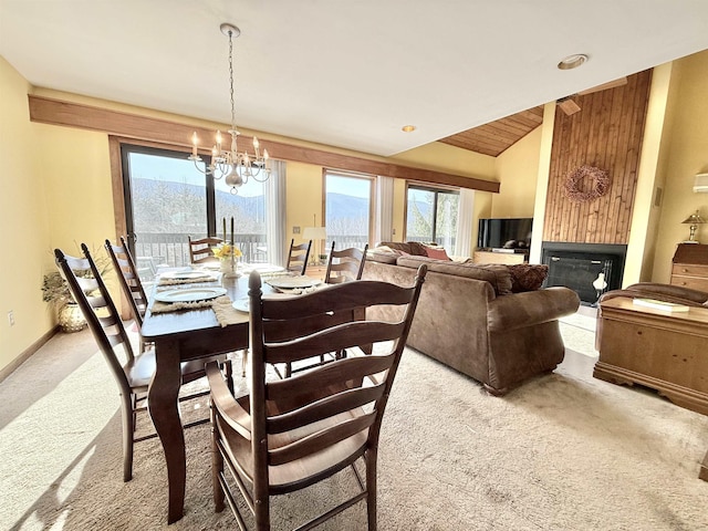 carpeted dining space with lofted ceiling, a large fireplace, baseboards, and a chandelier